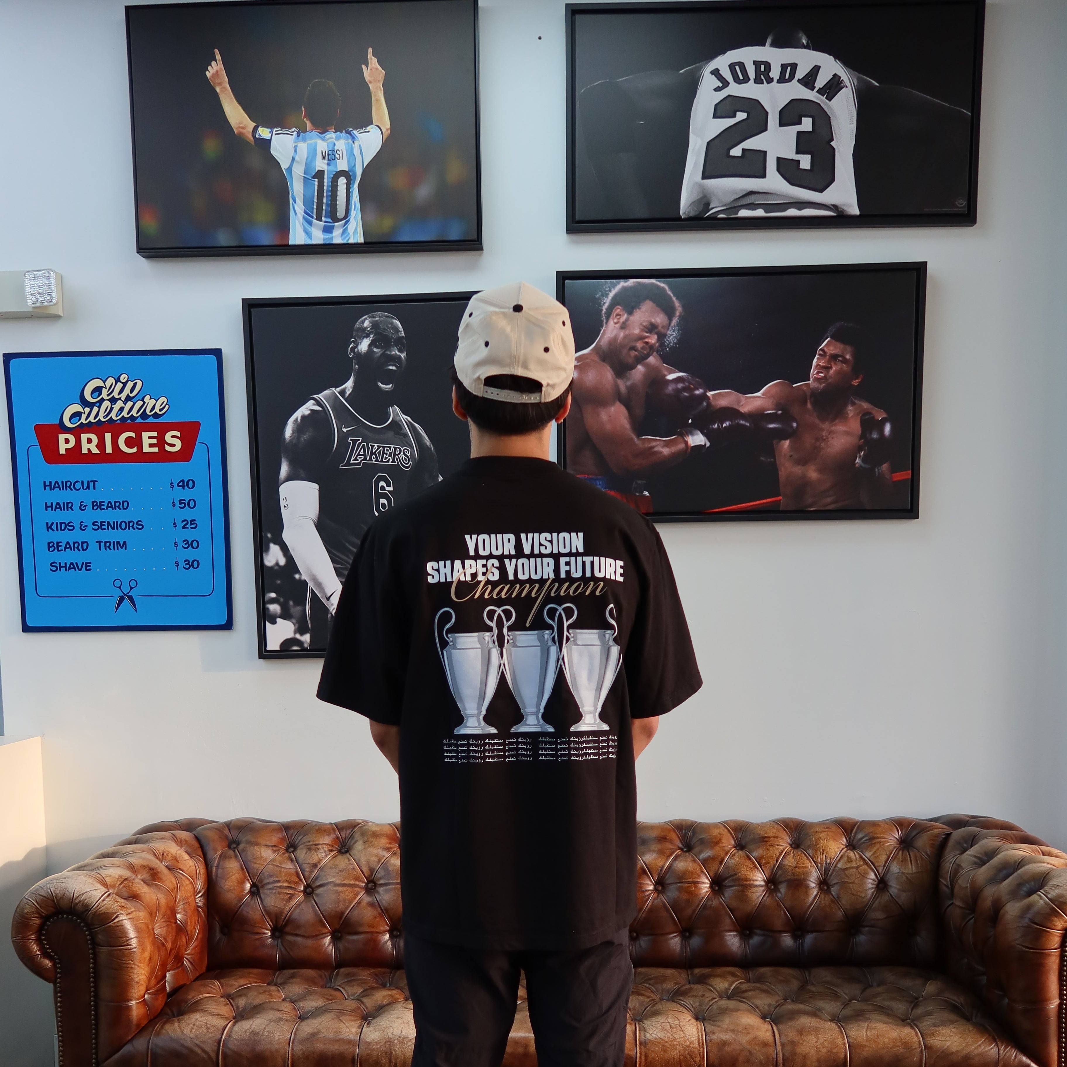 Person wearing a black tee with graphic designs, standing in a room with posters and a brown couch.